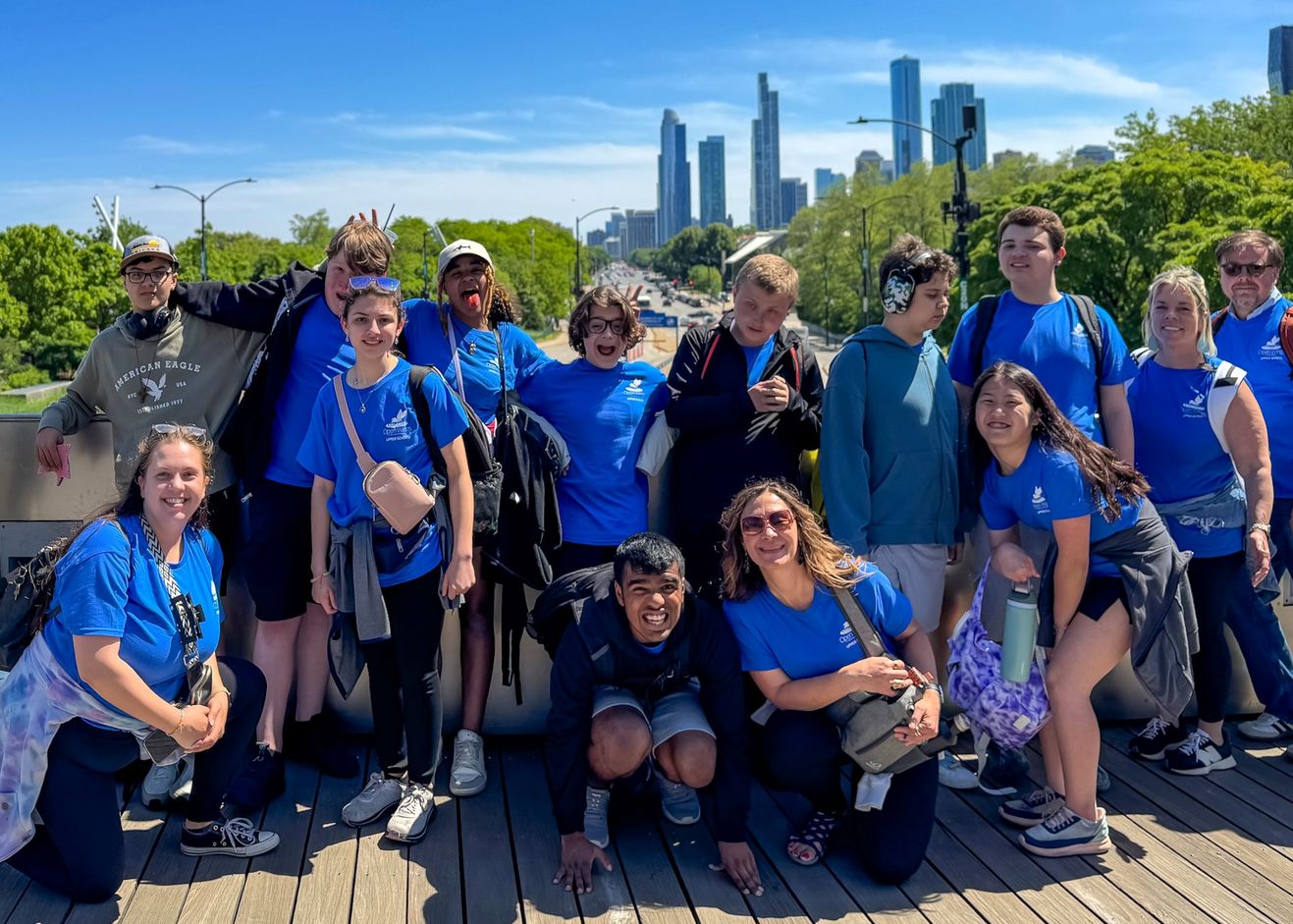 Students and staff in matching blue Open Wings shirts pose together on a bridge with the Chicago skyline behind them.