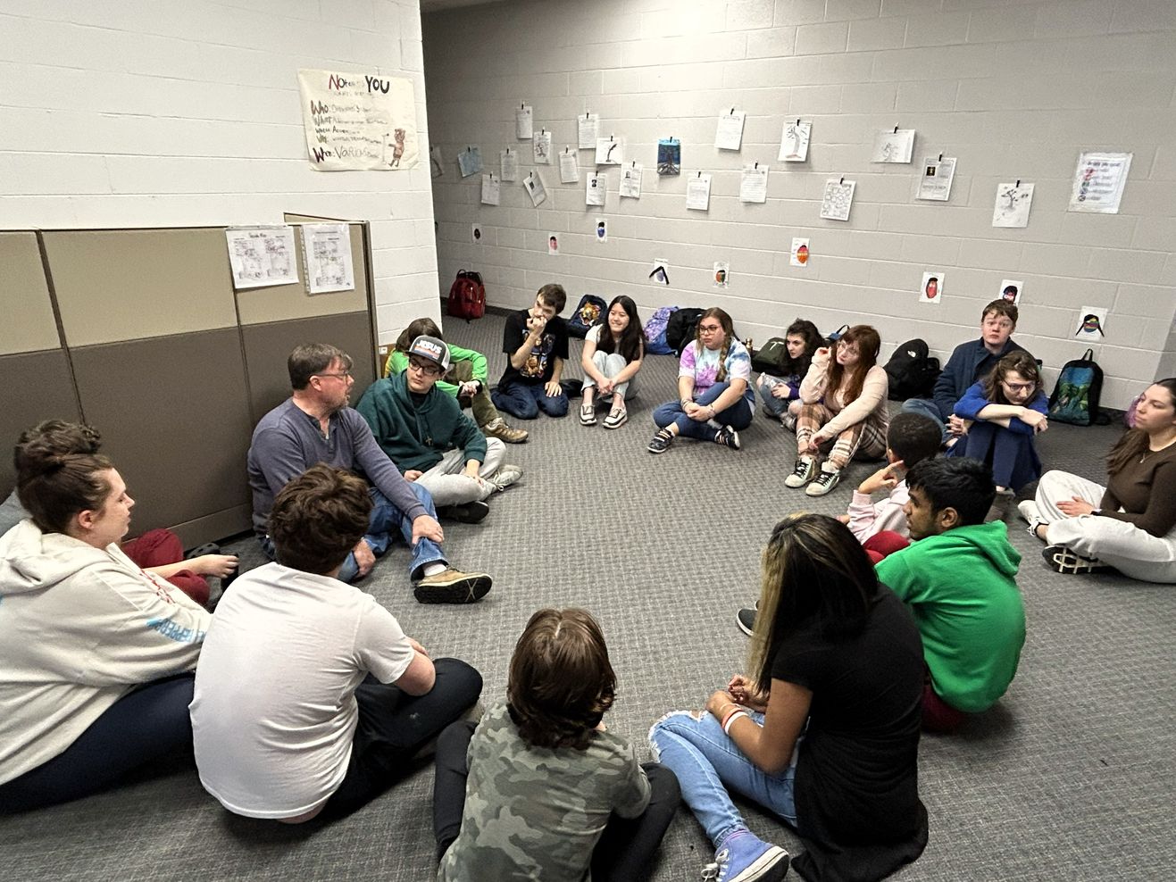 Upper School students and a teacher sit together in a circle on the classroom floor during a group discussion.